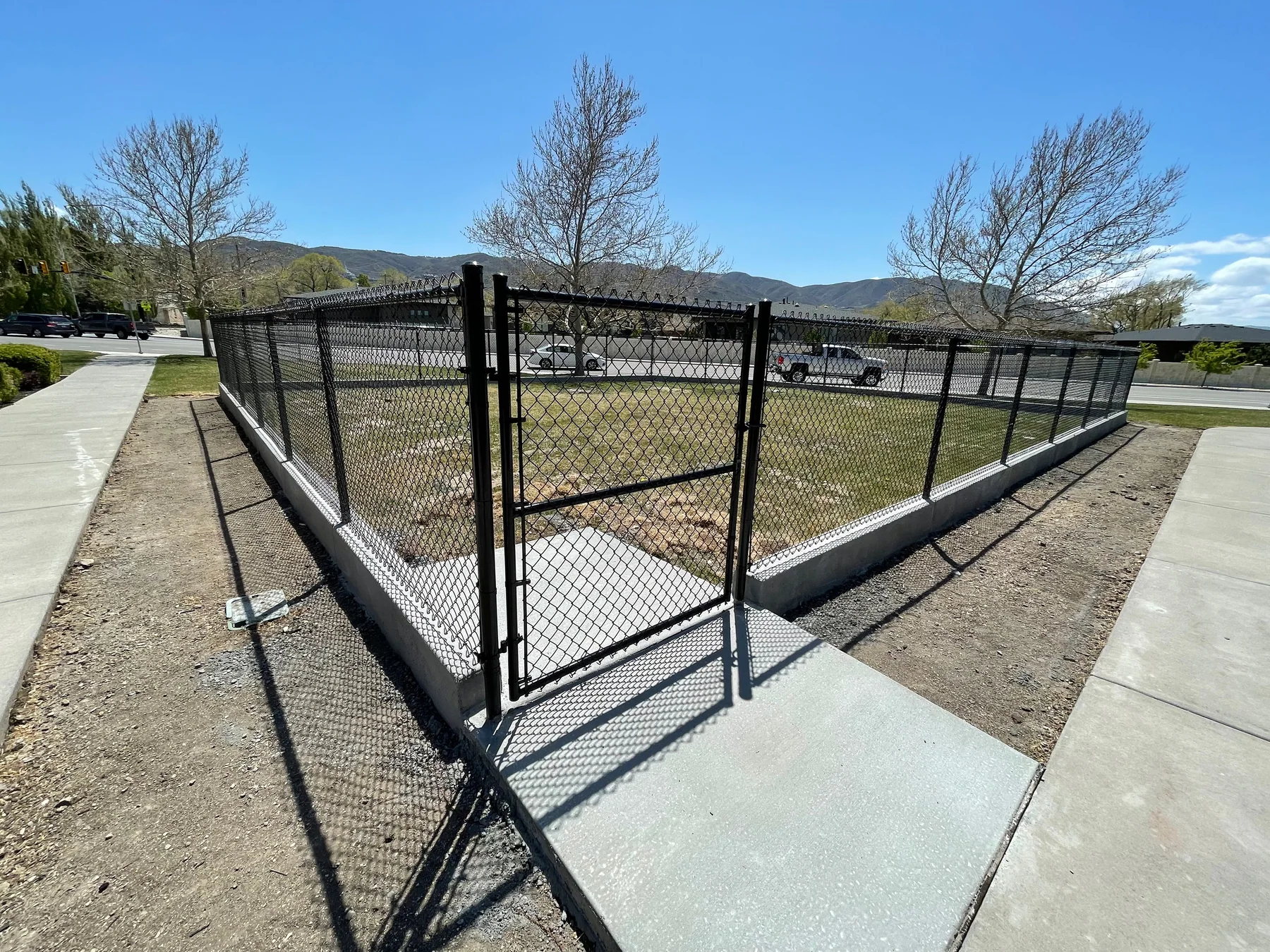 Black chain-link corner and access gate installed along a Utah sidewalk