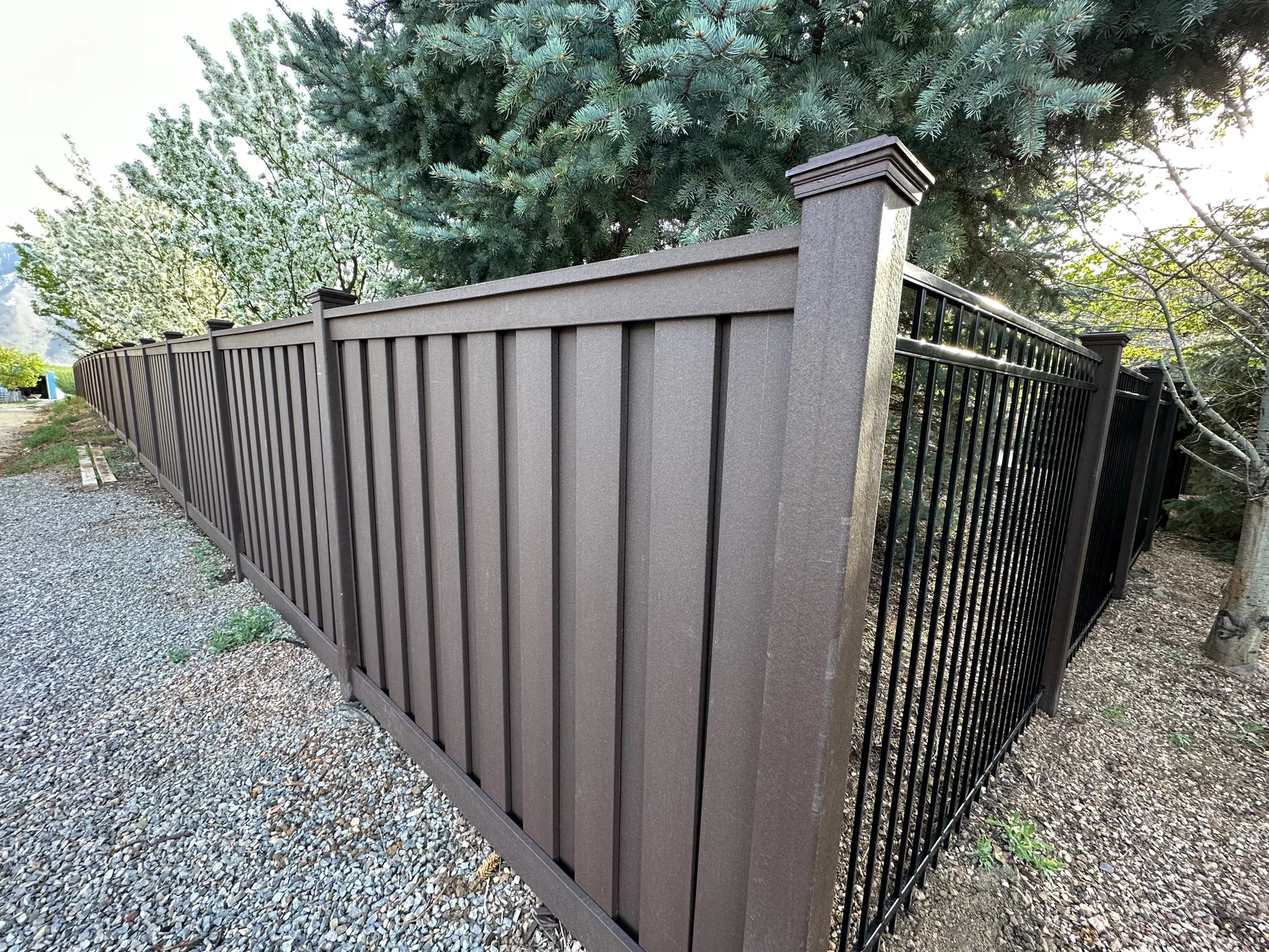 Brown Trex composite privacy fence meeting a black ornamental iron gate at a Utah property