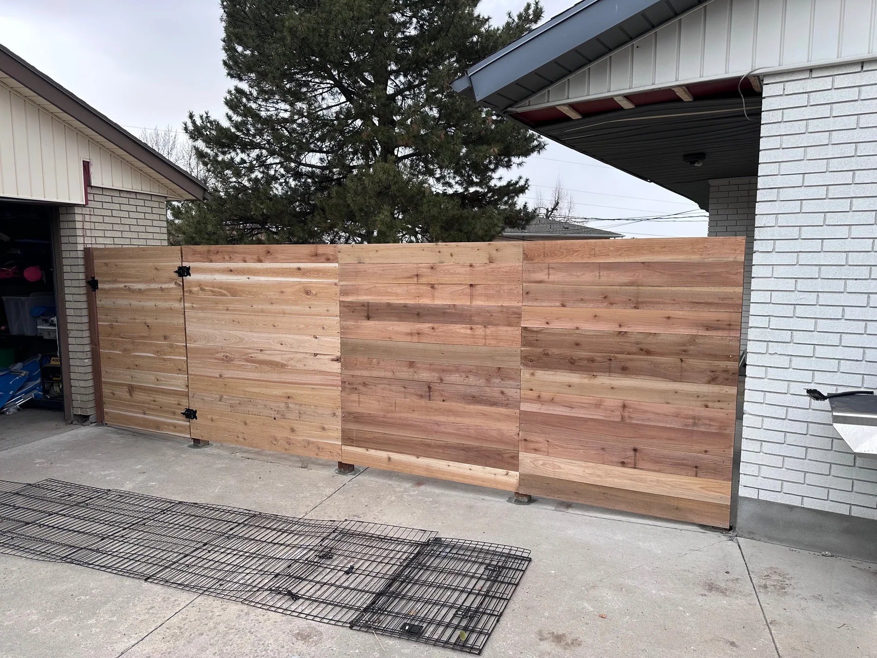 Modern horizontal cedar driveway gate installed beside a white brick Utah home