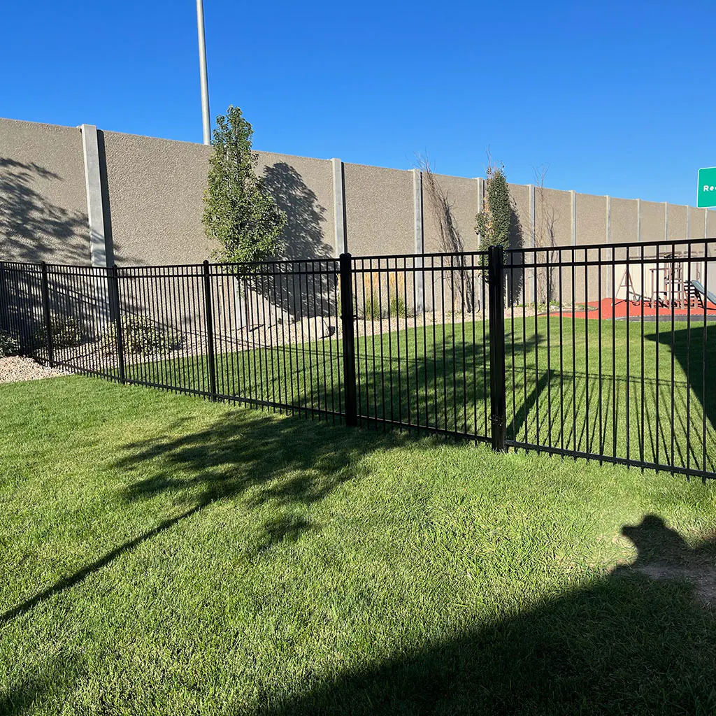 Long black ornamental iron fence beside a commercial sound wall in Utah County