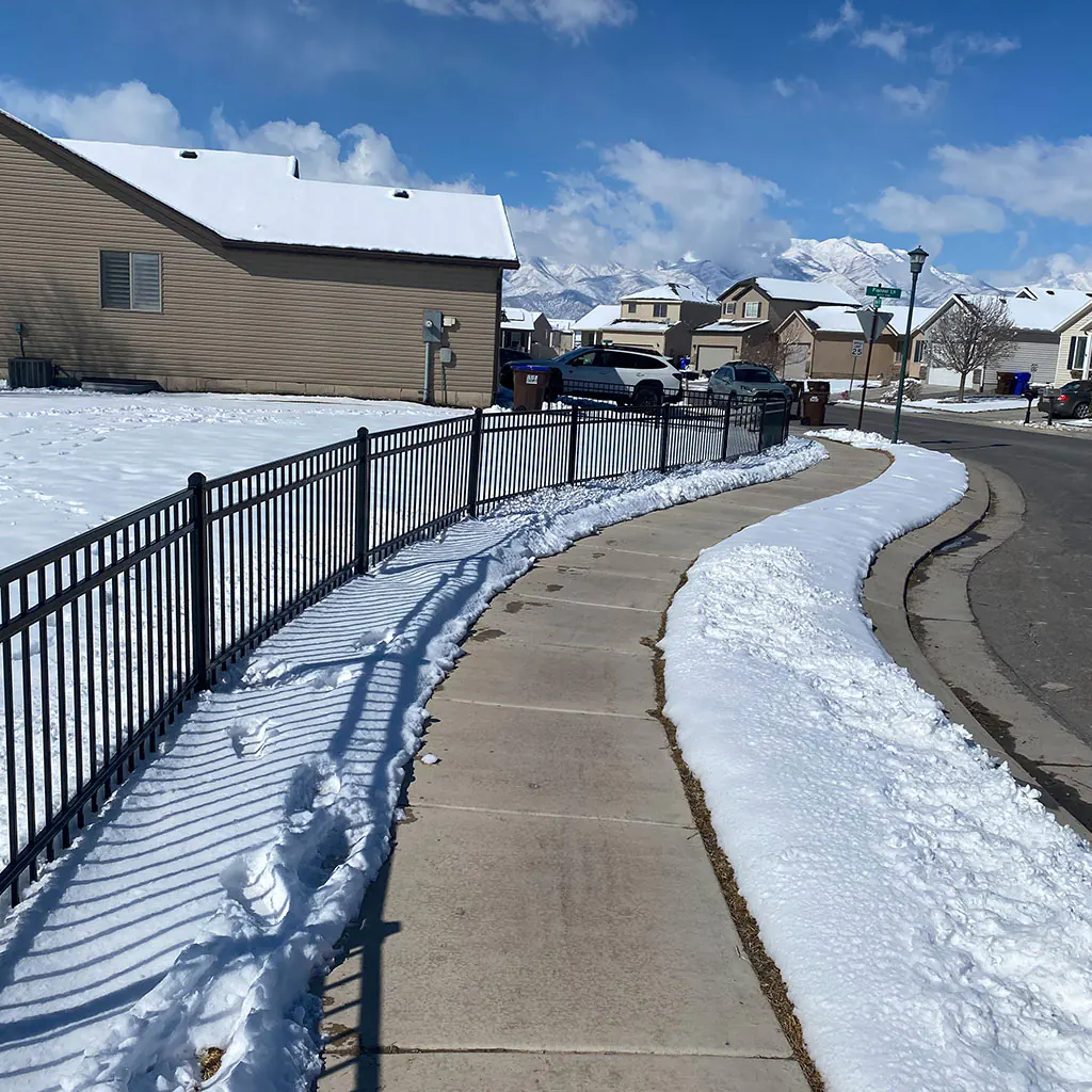 Black ornamental iron fence curving along a snowy Utah County sidewalk